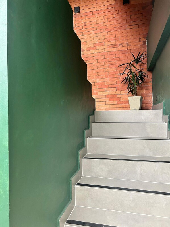 A staircase with a green wall on one side and a brick wall on the other, leading to a landing where a potted plant is placed.