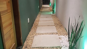A narrow hallway with a pebble path, wooden door, and green walls. - Morada do Sol Suítes - Suíte 06 (Arraial do Cabo)