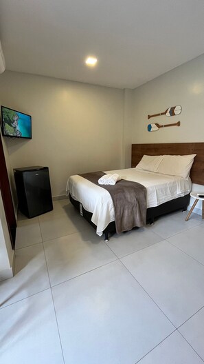 A hotel room with a bed, a flat-screen TV, a small refrigerator, and a wall-mounted artwork.