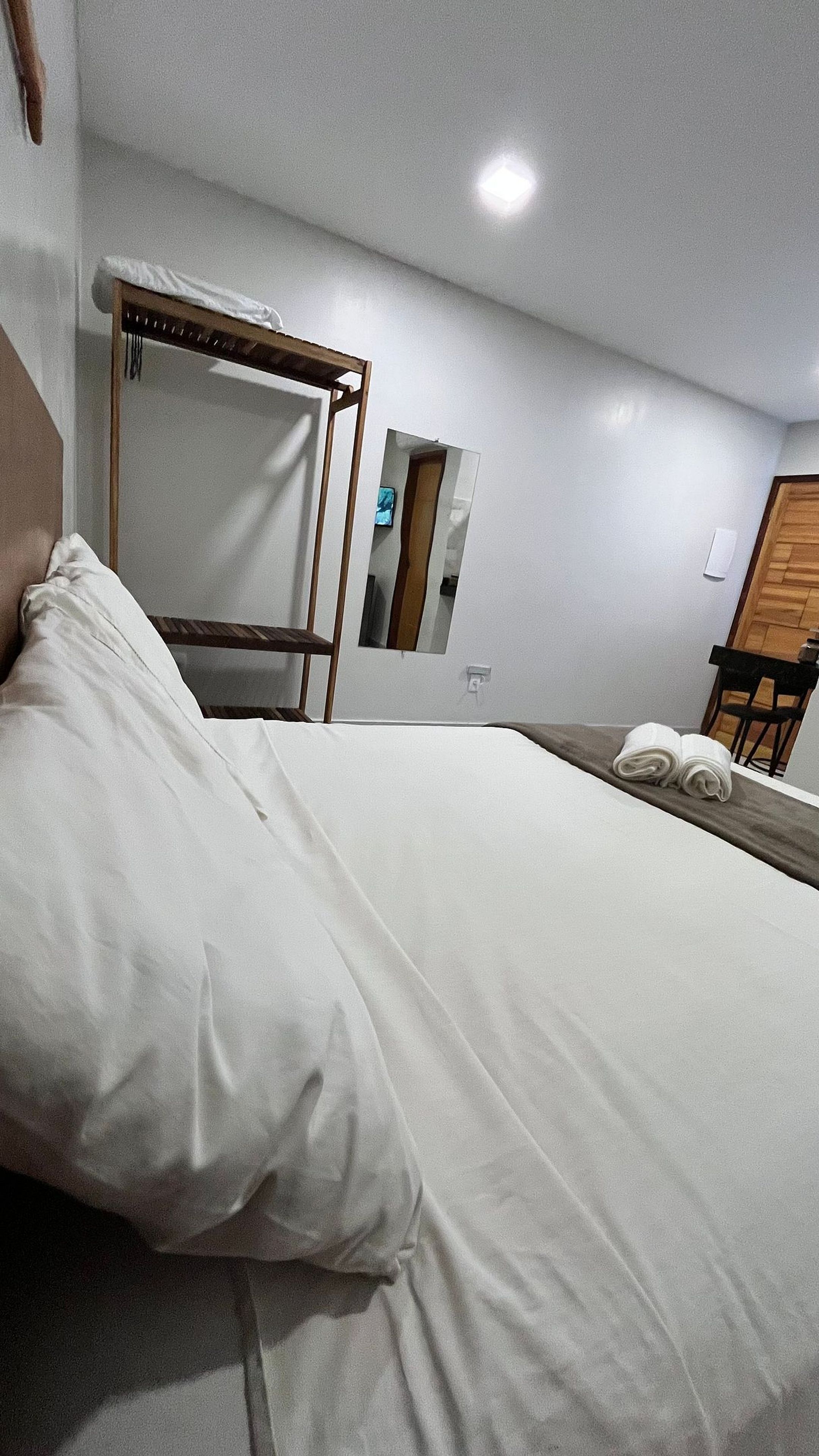 A hotel room with a bed, a wooden headboard, a mirror, and a wooden chair.