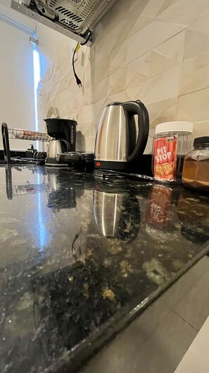 A kitchen counter with a kettle, a coffee maker, and a jar of spices. - Morada do Sol Suítes - Suíte 07 (Arraial do Cabo)