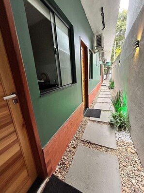 A narrow hallway with a green wall, wooden door, and a window. - Morada do Sol Suítes - Suíte 07 (Arraial do Cabo)