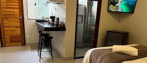 A hotel room with a bed, a TV, a kitchenette, and a bathroom.