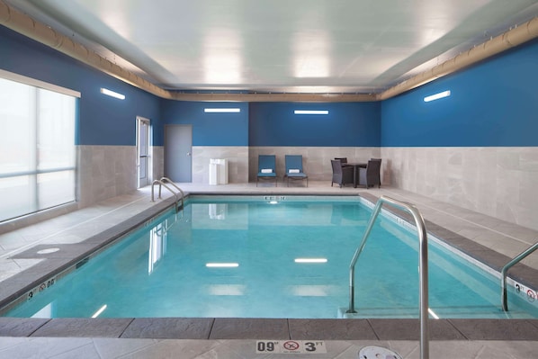 Una piscina interior con agua cristalina, paredes con azulejos y techo con conductos a la vista.
