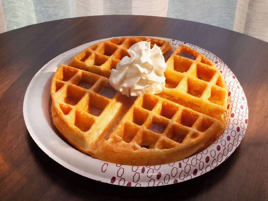 A waffle with whipped cream on a patterned plate on a wooden table.