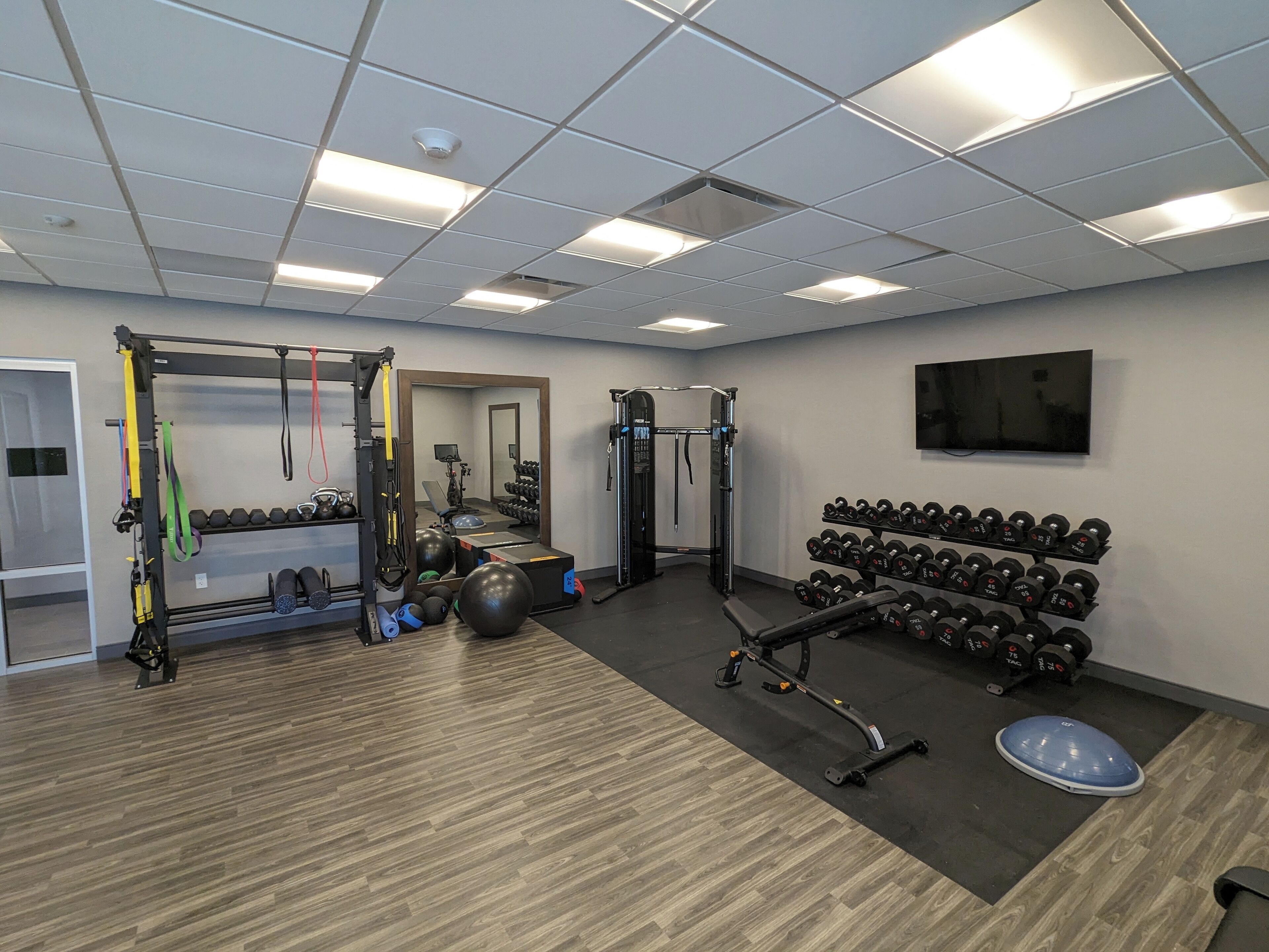 A gym with exercise equipment, a mirror, and a TV on the wall.