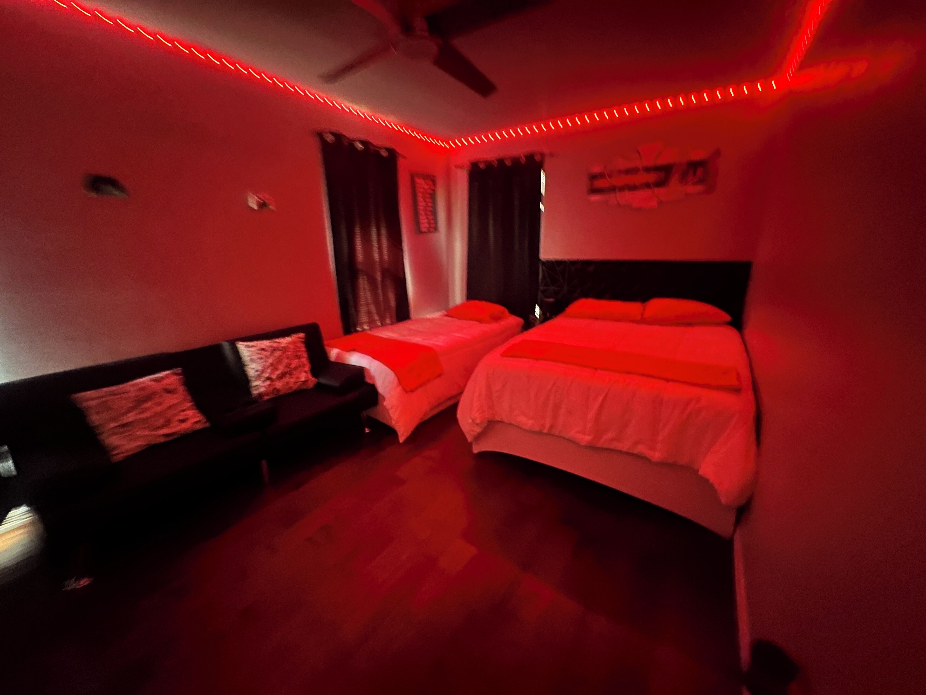 Ein Zimmer mit zwei Betten, einer Schlafcouch und roter LED-Beleuchtung.