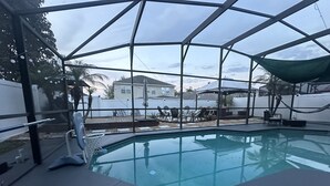 Ein Innenpool mit freiem Blick auf den Garten, einschließlich einer Terrasse mit Stühlen und einem Tisch.