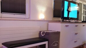 A room with a white bench, a television on a stand, a laundry bag, and a white dresser with drawers. - Gemütliche Ferienwohnung in Bühler (Bühler)
