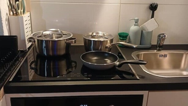 A kitchen with a stove, pots, a frying pan, a sink, and various utensils. - Gemütliche Ferienwohnung in Bühler (Bühler)