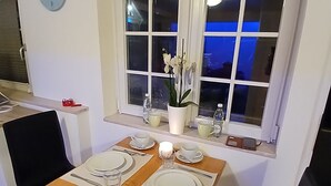 A dining area with a wooden table set for two, two chairs, a potted orchid, and a clock on the wall. - Gemütliche Ferienwohnung in Bühler (Bühler)