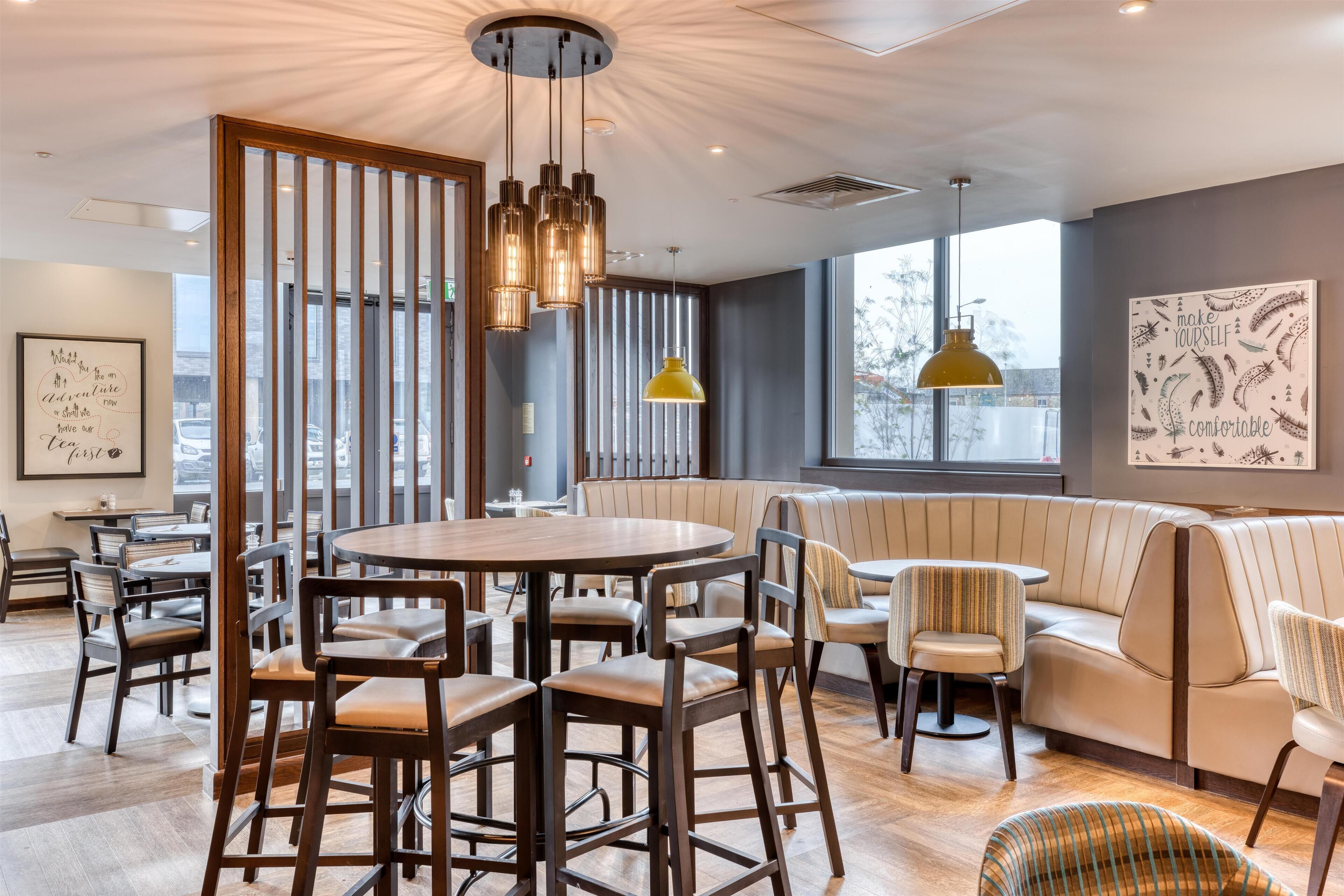 A modern interior with a round table, bar stools, a sofa, and a yellow pendant light.