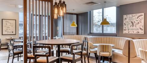 A modern interior with a round table, bar stools, a sofa, and a yellow pendant light.