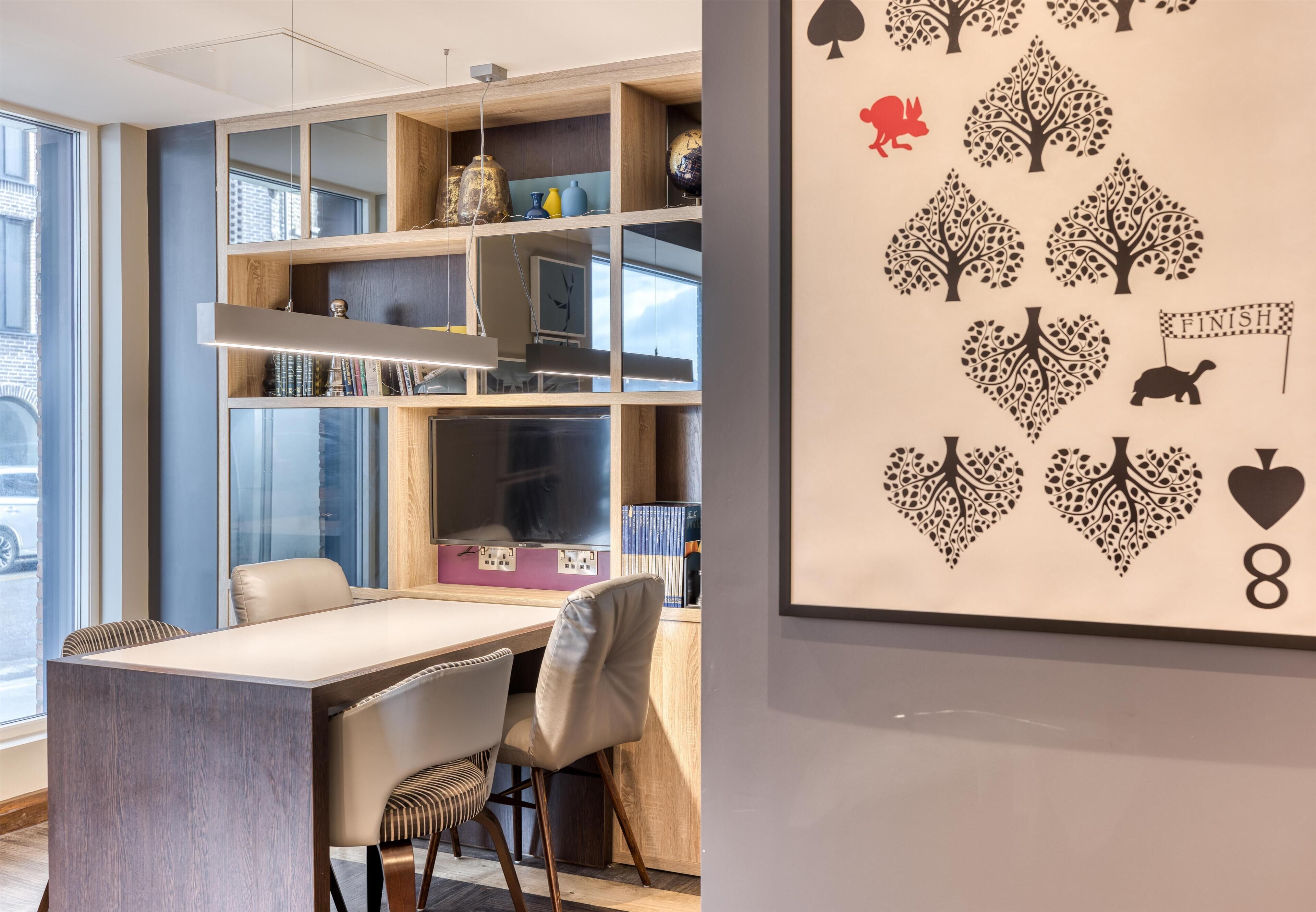 Una camera moderna con un tavolo da pranzo, sedie, una libreria e una parete decorata con un motivo a carte da gioco.