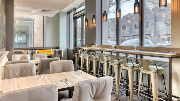 A modern restaurant interior with high tables, bar stools, and large windows offering views of the city. - Premier Inn Dublin Cc The Liberties (Dublin)