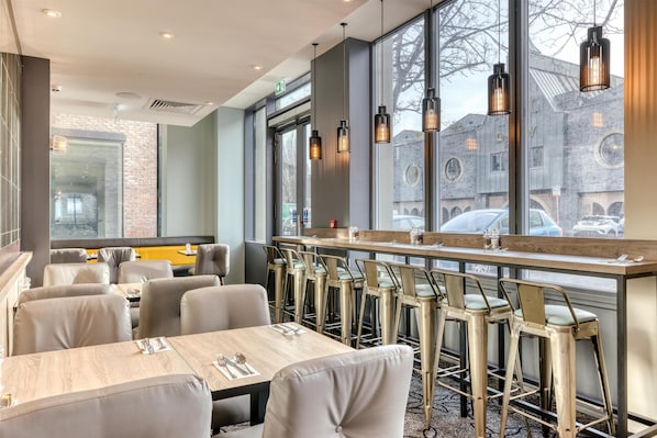 A modern restaurant interior with high tables, bar stools, and large windows offering views of the city. - Premier Inn Dublin Cc The Liberties (Dublin)