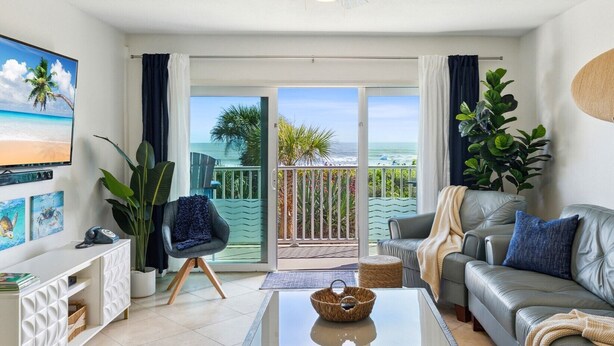 A modern living room with a balcony, a television, and a sofa. - 2BD/2BA Cocoa Beach Oceanfront + POOL & ALL of Downtown! (Cocoa Beach)