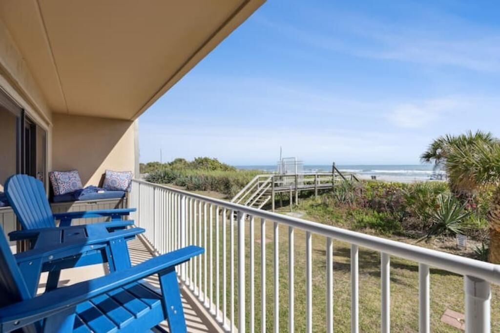 A balcony with blue chairs and a view of the beach.