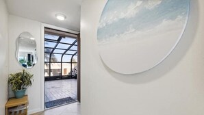 A hallway with a large circular wall art, a potted plant, and a wooden bench. - 2BD/2BA Cocoa Beach Oceanfront + POOL & ALL of Downtown! (Cocoa Beach)