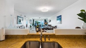 A modern kitchen with a granite countertop, stainless steel sink, and a dining area with a table and chairs. - 2BD/2BA Cocoa Beach Oceanfront + POOL & ALL of Downtown! (Cocoa Beach)