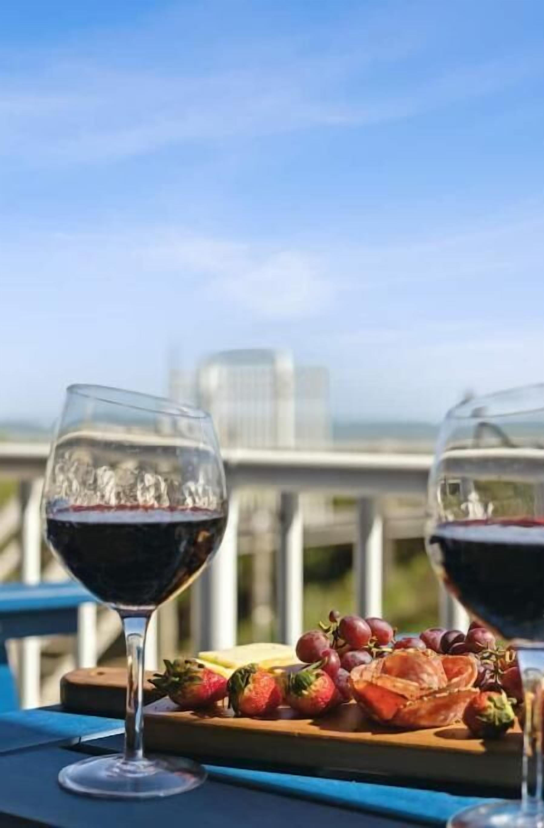 Una mesa con dos copas de vino y una bandeja de frutas en un balcón con vista a la ciudad.