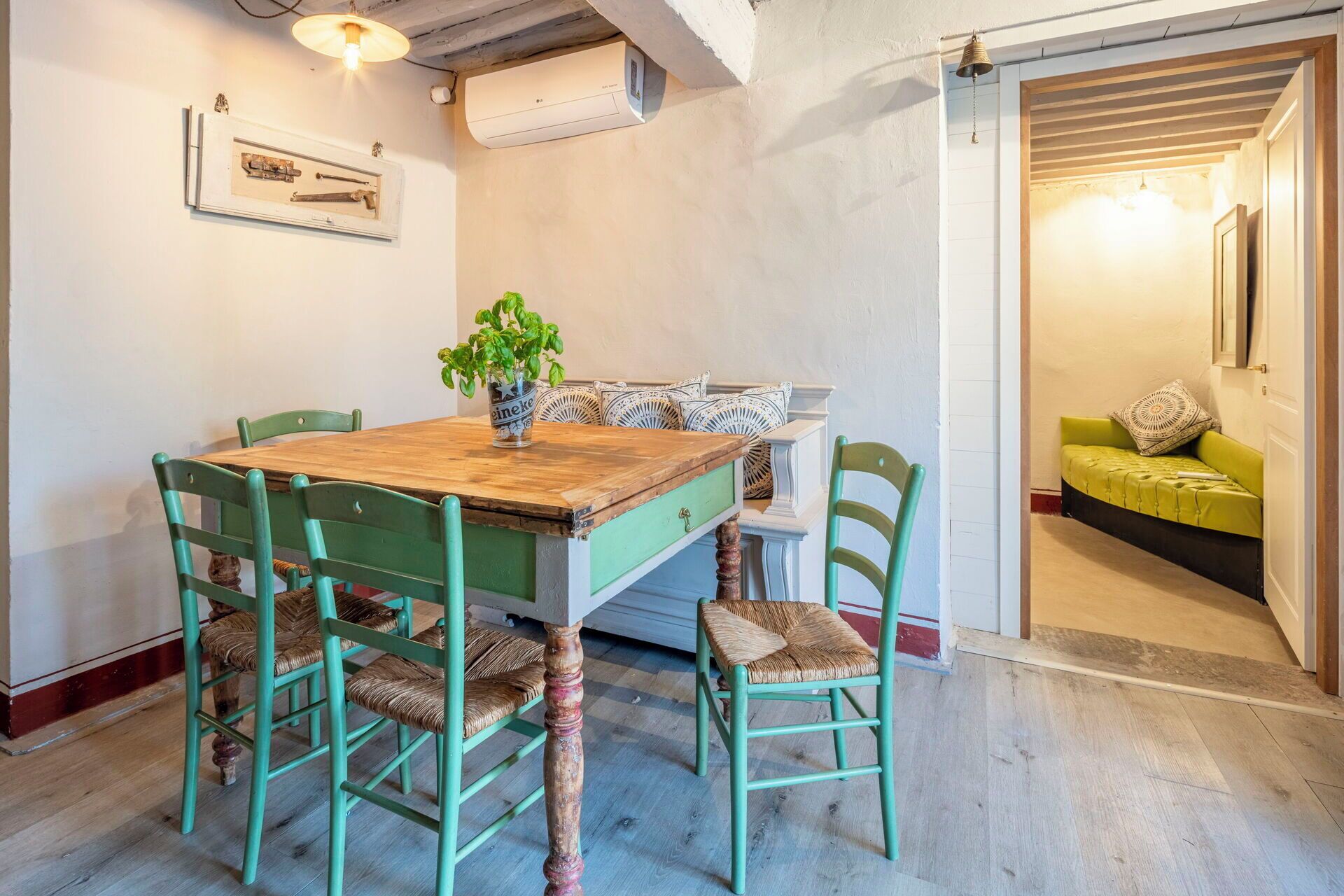 Un'area pranzo con un tavolo in legno, quattro sedie verdi, una pianta in vaso e un condizionatore d'aria a muro.
