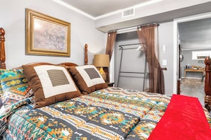 A bedroom with a bed, pillows, a framed picture, a lamp, and a door leading to another room.