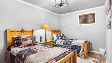Ein Schlafzimmer mit zwei Holzbetten, einem Nachttisch mit Lampe, einem Fenster mit Jalousien und einem Deckenventilator.