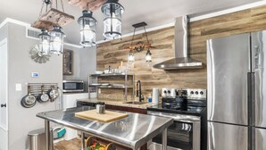 Une cuisine moderne dotée d’appareils électroménagers en acier inoxydable, d’éléments décoratifs en bois et de luminaires suspendus.