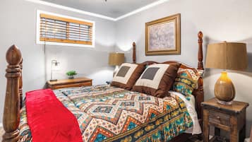 A bedroom with a bed, bedside tables, a lamp, a window with blinds, and a framed picture on the wall.