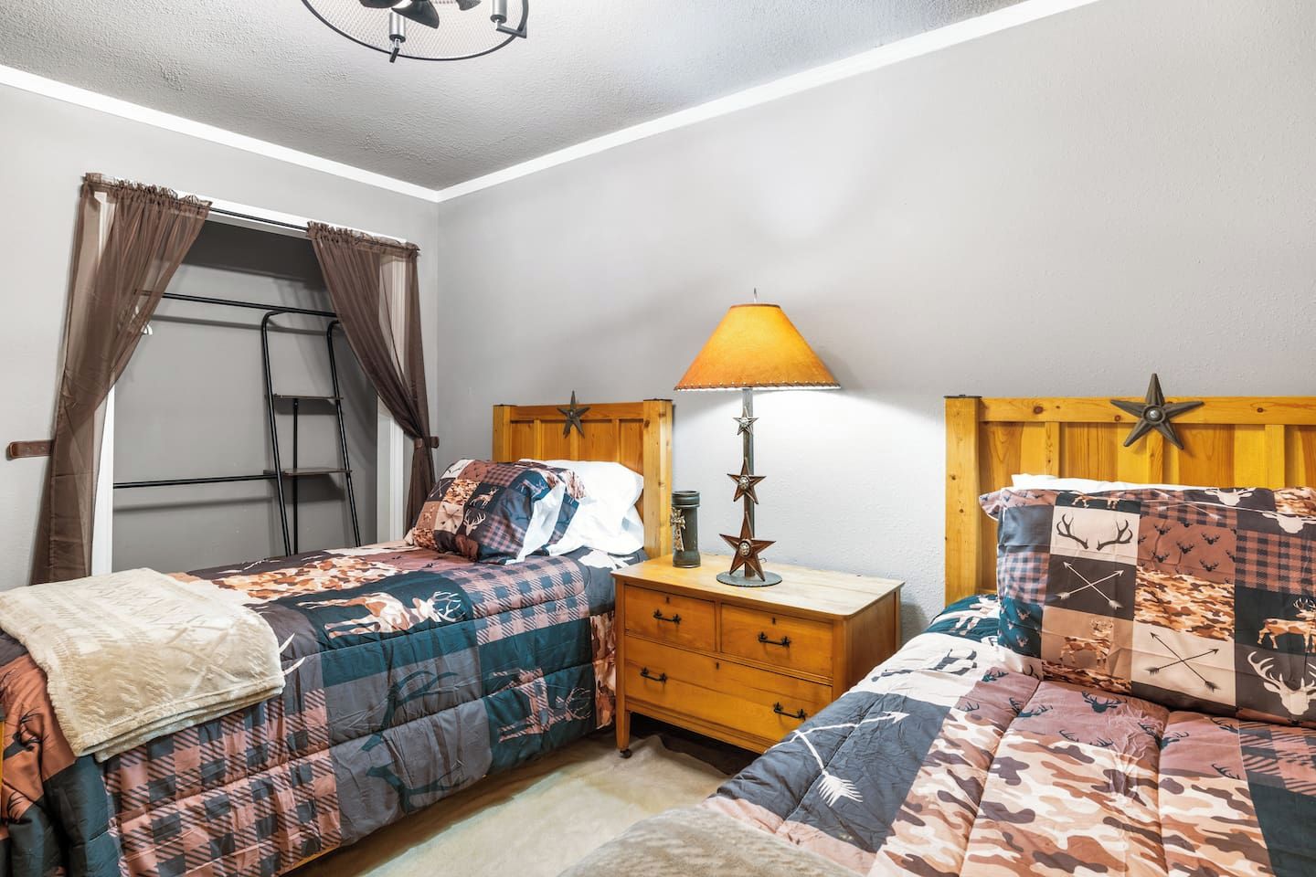 A bedroom with two beds, a nightstand, a lamp, and a window with curtains.