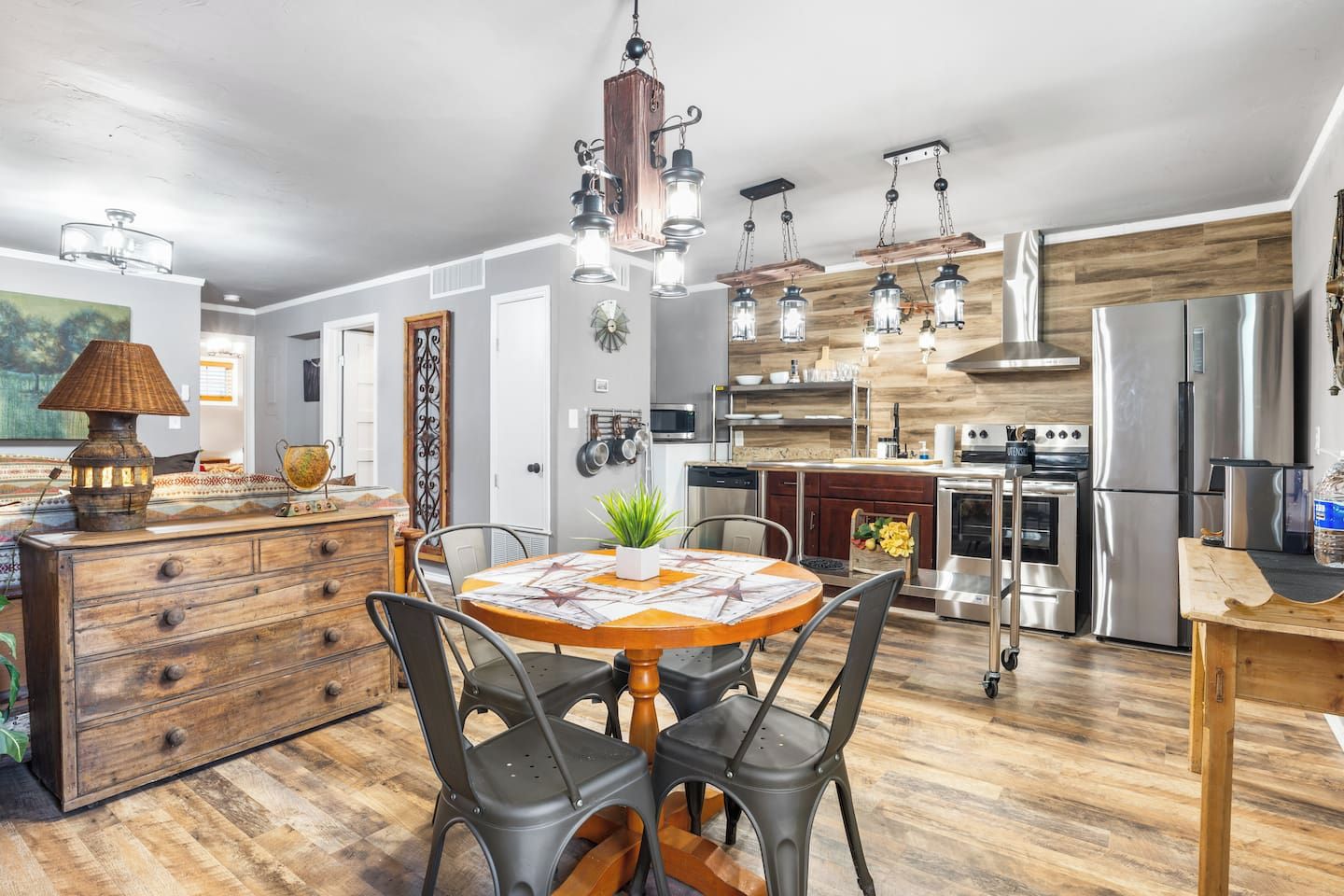 A modern kitchen with stainless steel appliances, a wooden dining table, and a chandelier.