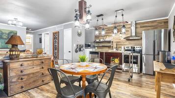A modern kitchen with stainless steel appliances, a wooden dining table, and a chandelier.