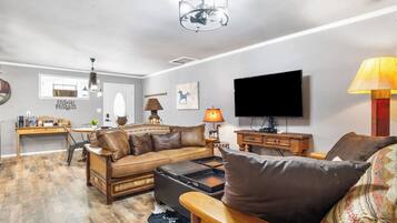 A living room with a sofa, coffee table, TV, and a dining area with a table and chairs.