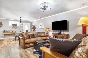 A living room with a sofa, coffee table, TV, and a dining area with a table and chairs. - Salt Block - The Rustic 1 | Cozy 2BR in Bandera (Bandera)