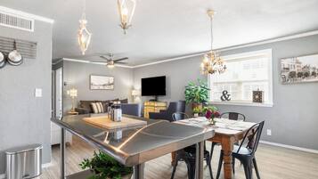 A modern kitchen with a central island, dining area with chairs, a sofa, and a TV in the living room.