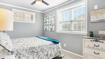 A bedroom with a bed, a dresser, a ceiling fan, and two windows with blinds.