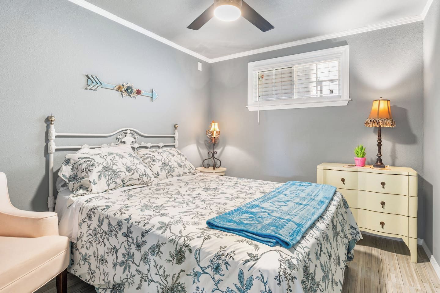 A bedroom with a bed, bedside table, lamp, dresser, and a decorative arrow on the wall.