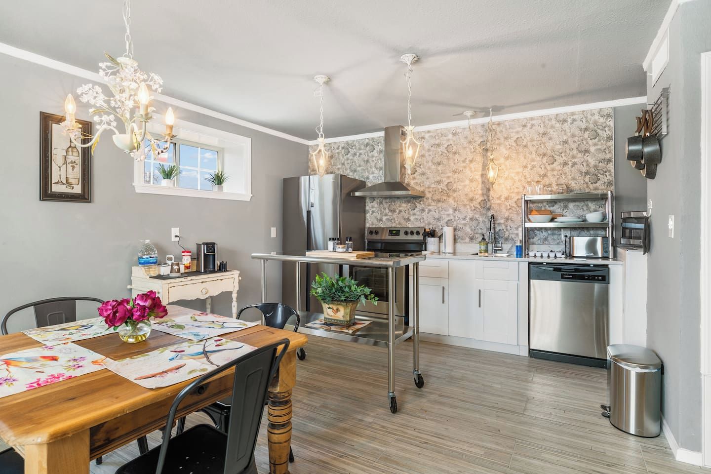 A modern kitchen with a dining area, stainless steel appliances, and a chandelier.