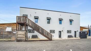 A building with a wooden staircase leading to a door, a fenced area, and a parking lot.