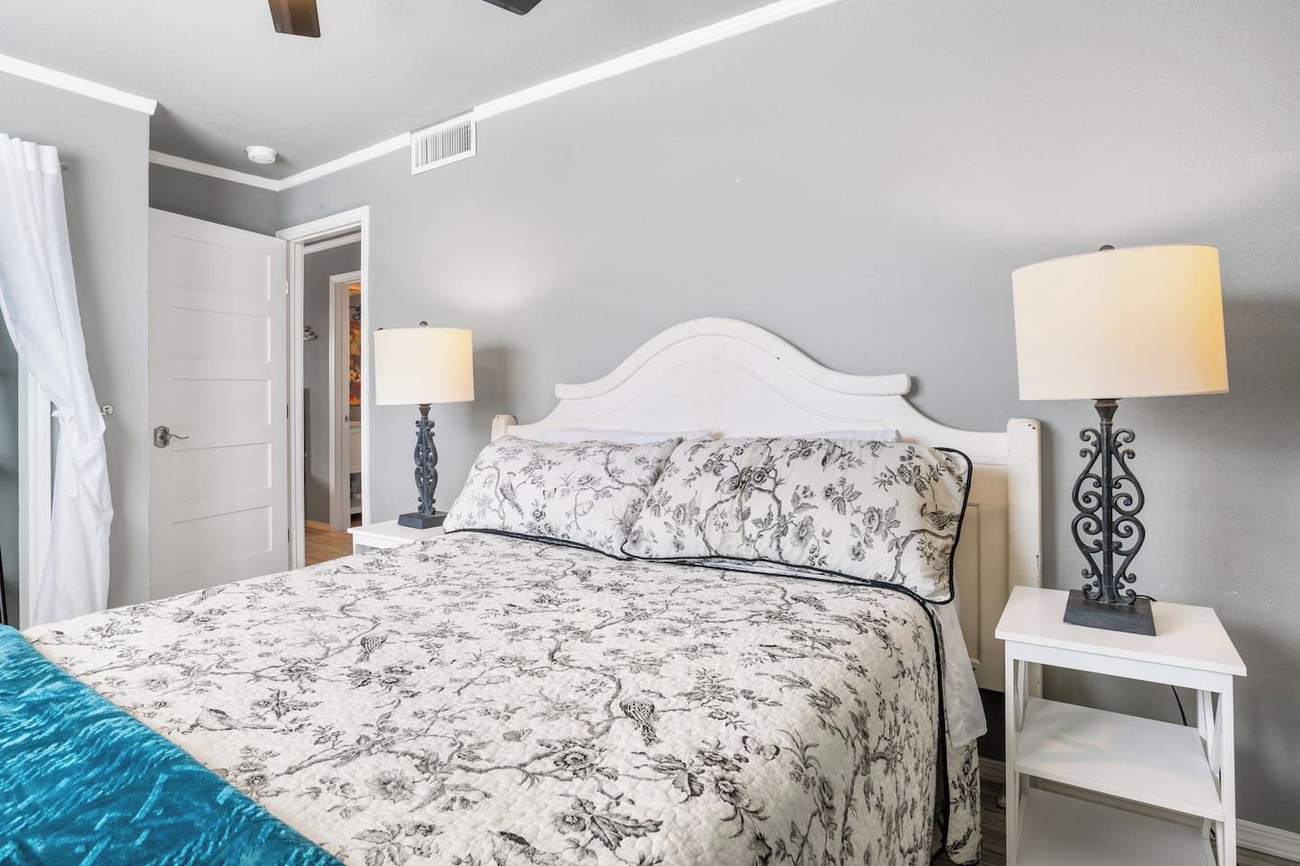Un dormitorio con cama, dos lámparas de noche, una puerta y una mesita de noche blanca.