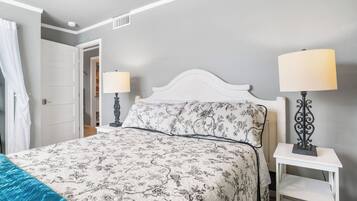 Un dormitorio con cama, dos lámparas de noche, una puerta y una mesita de noche blanca.