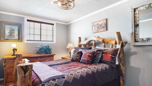 Una camera da letto con una testiera in legno rustico, un'ampia finestra con persiane, un comodino con una lampada e un quadro incorniciato appeso al muro.