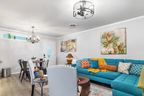 A living room with a blue sofa, a dining table with chairs, a chandelier, and artwork on the walls. - Salt Block-Santa Fe 5 | Walk to 11th St| 2BR Suite (Bandera)