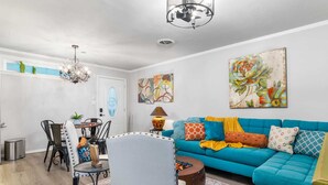 Een moderne woonkamer met een blauwe bank, een eettafel met stoelen, een kroonluchter en kunstwerken aan de muur.