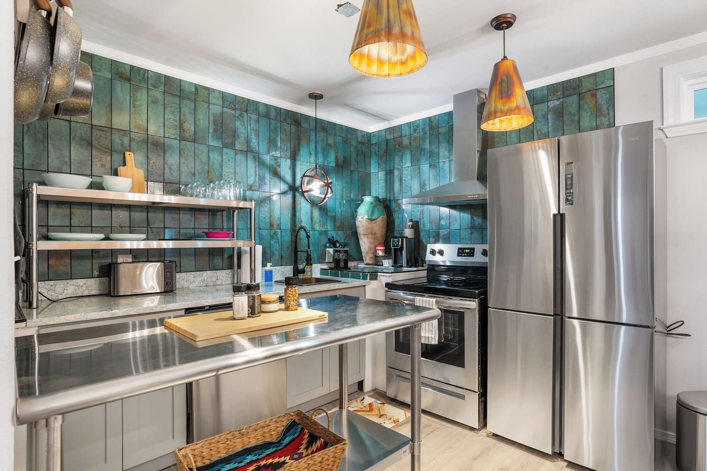 A modern kitchen with stainless steel appliances, a central island, and teal backsplash tiles.