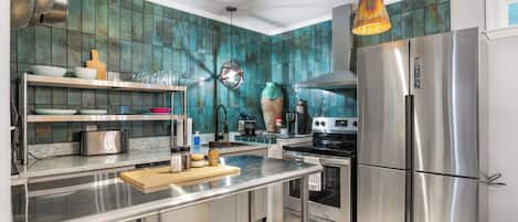A modern kitchen with stainless steel appliances, a central island, and teal backsplash tiles.