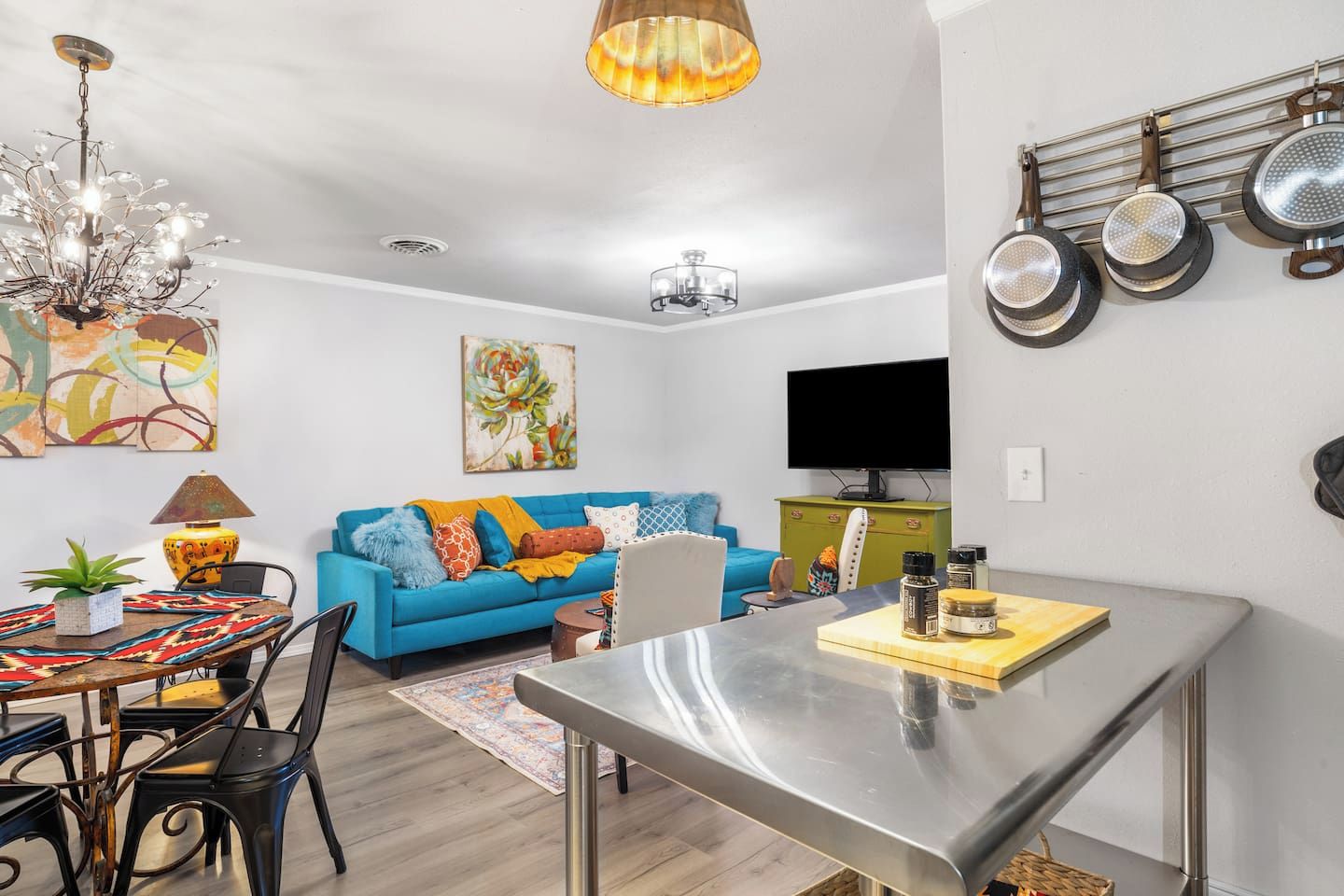 En moderne opholdsstue med spiseplads, sofa, fjernsyn og et køkken med ophængte gryder.