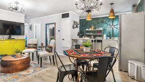 A modern kitchen with a central island, a dining area with a patterned tablecloth, and a living area with a television and colorful decor. - Salt Block-Santa Fe 5 | Walk to 11th St| 2BR Suite (Bandera)