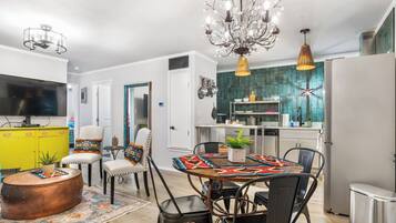 A modern kitchen with a central island, a dining area with a patterned tablecloth, and a living area with a television and colorful decor.